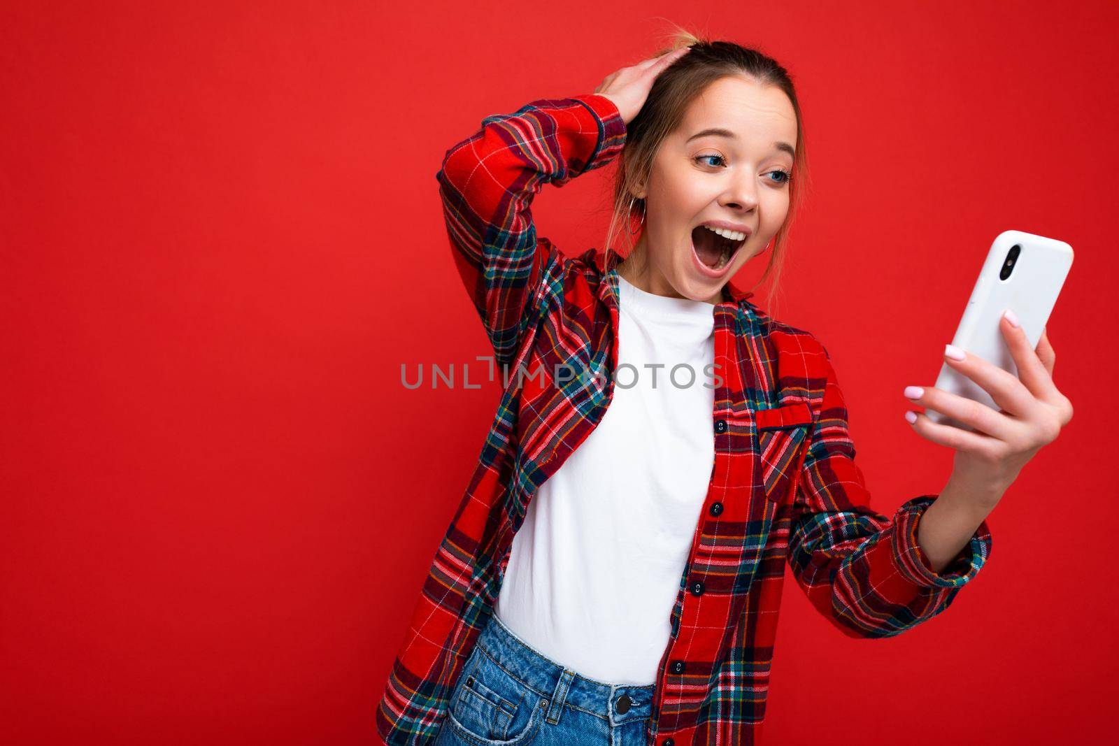 Photo of attractive crazy amazed surprised young woman wearing casual stylish clothes standing isolated over background with copy space holding and using mobile phone looking at device screen.
