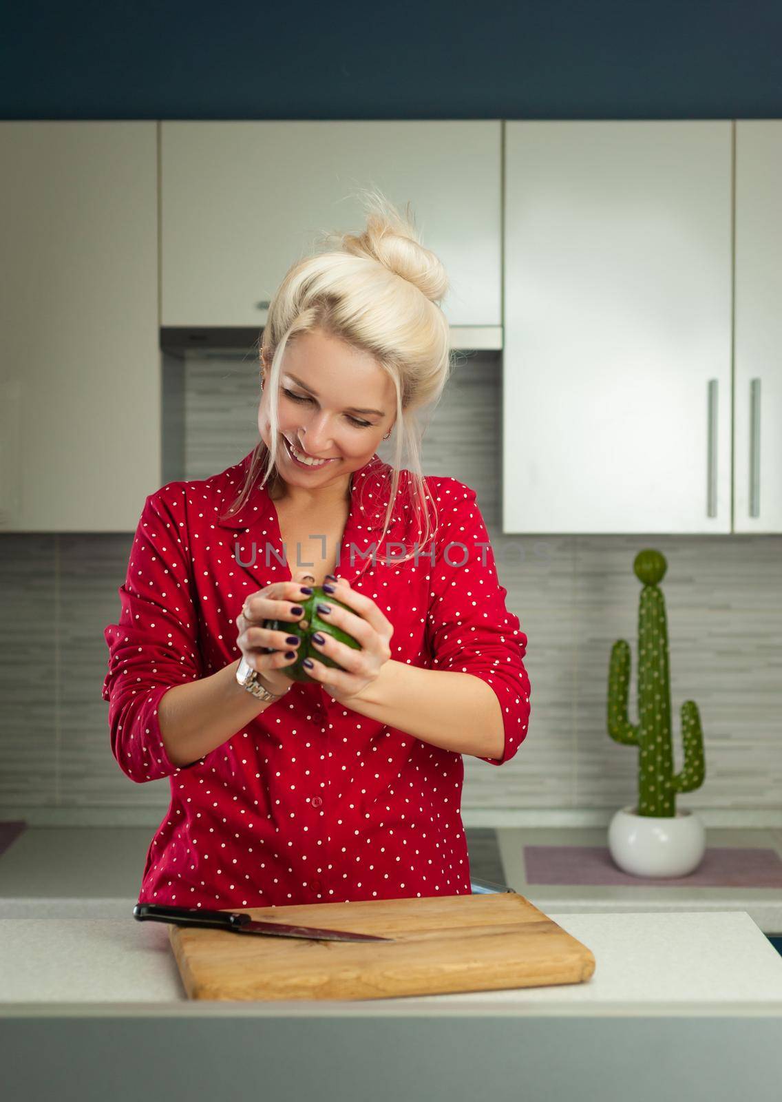 blonde vegan woman cuts avocado in kitchen by Rotozey