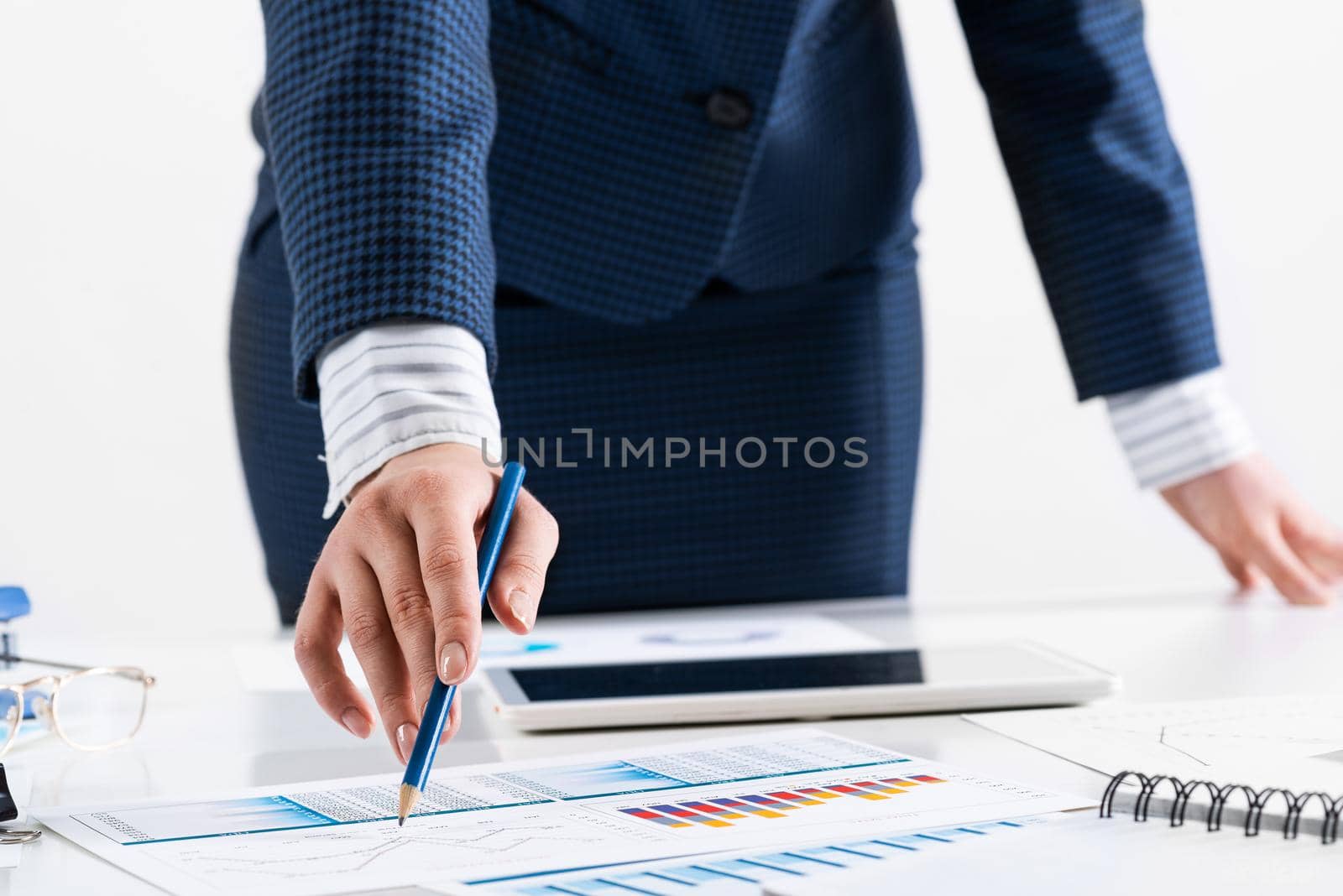 Businesswoman standing near office desk and analyzing financial charts. Successful corporate manager in business suit. Close-up woman hand with pen. Business presentation in conference room