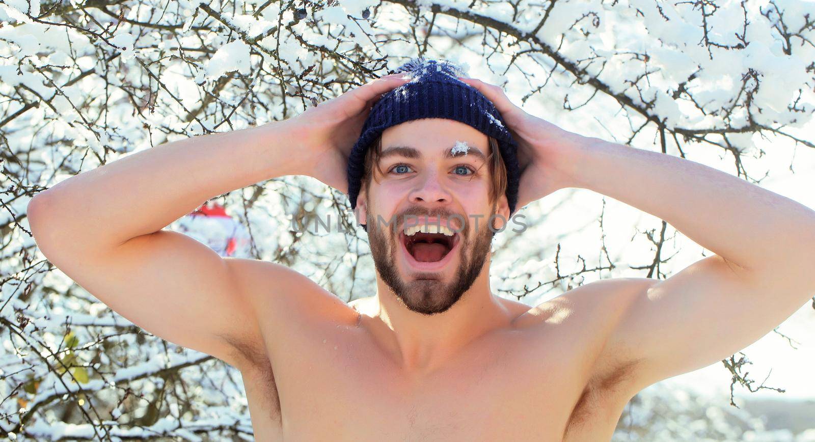 Excited young man or sexy muscular guy with bare torso and chest on fit body in winter park outdoor.