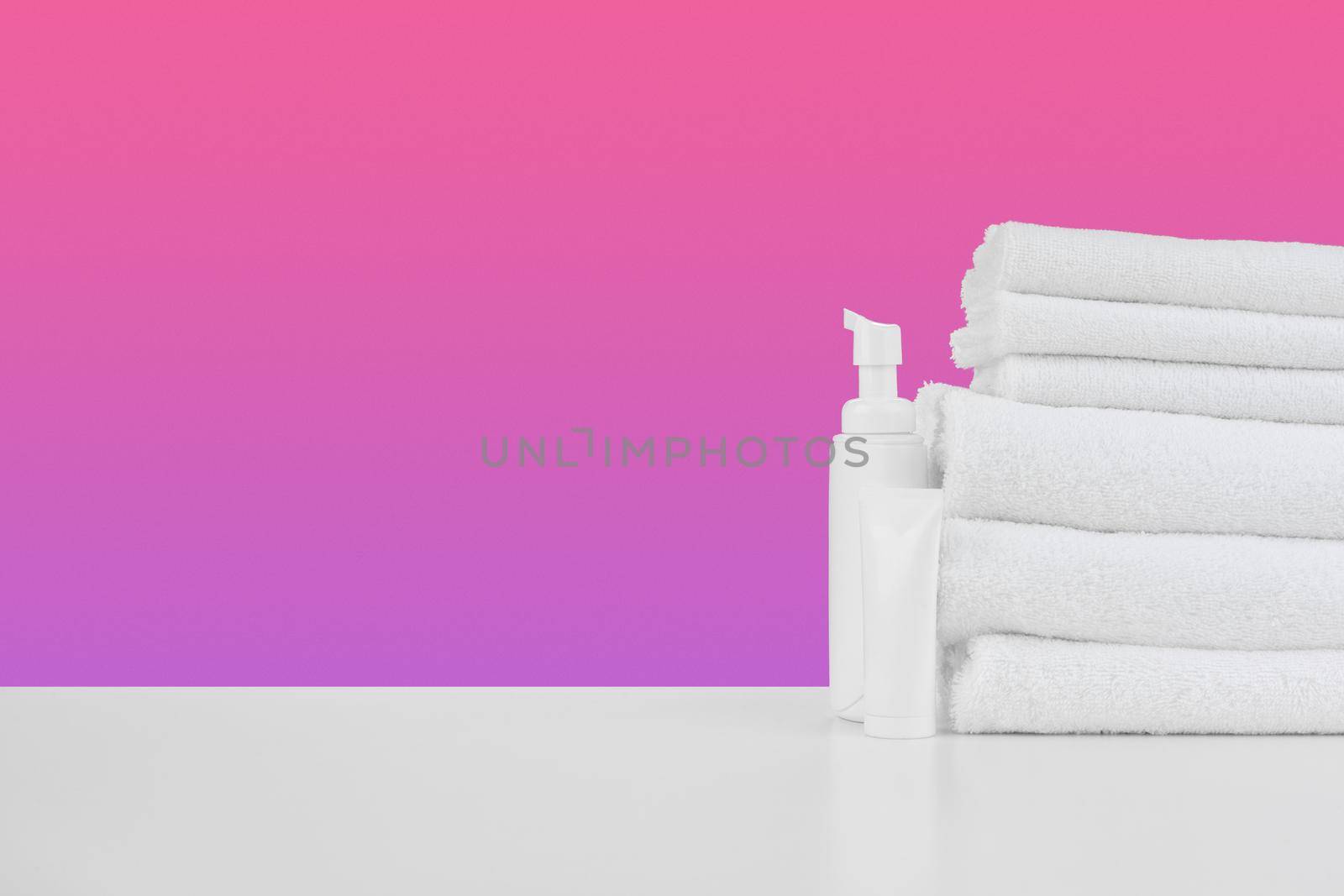 Pile of towels, bottles with shampoo on white table isolated