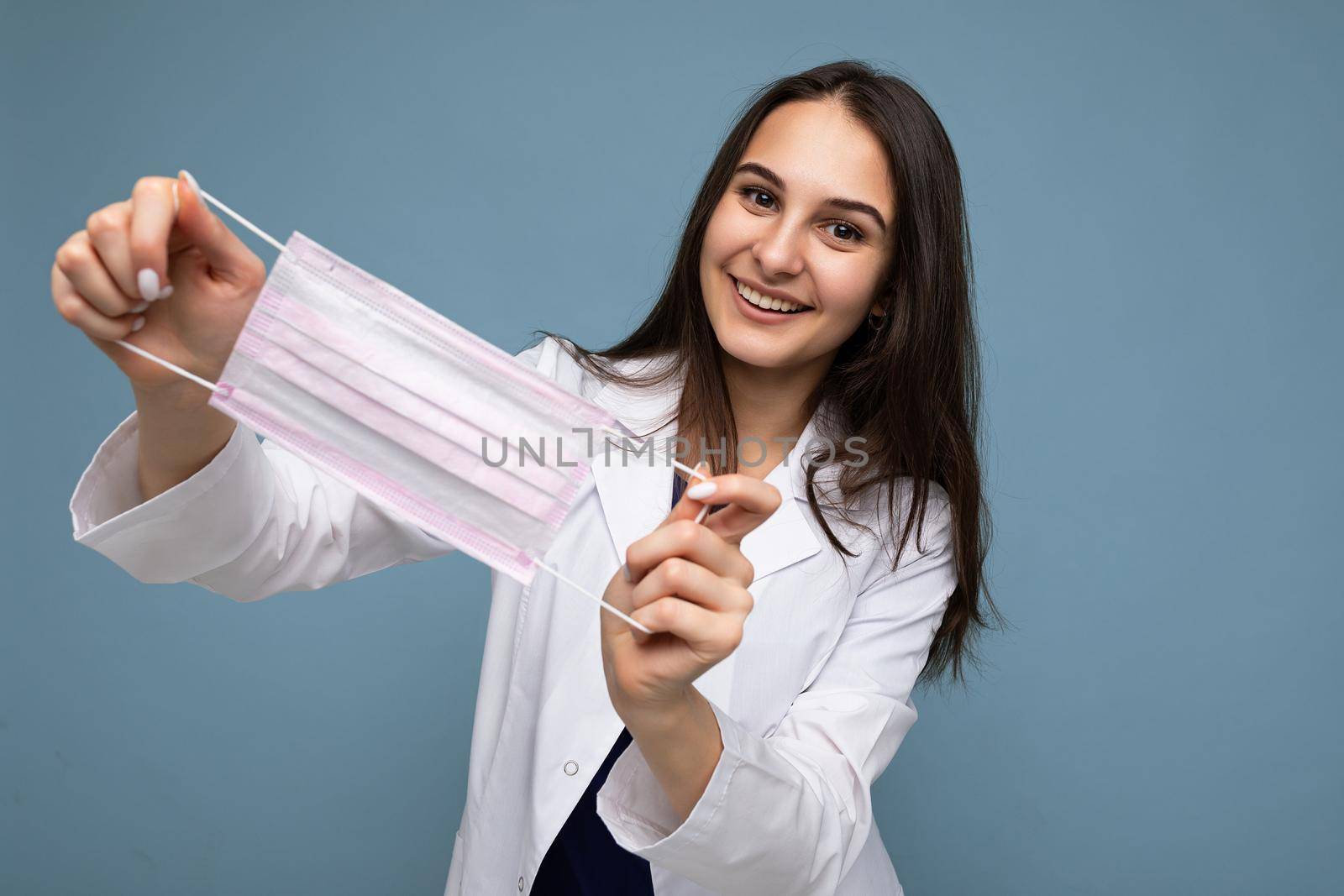 Happy young woman holds and wears a white medical mask to protect yourself from corona virus, cares for her health and safety, sticks to self-isolation. Concept of Covid-19.