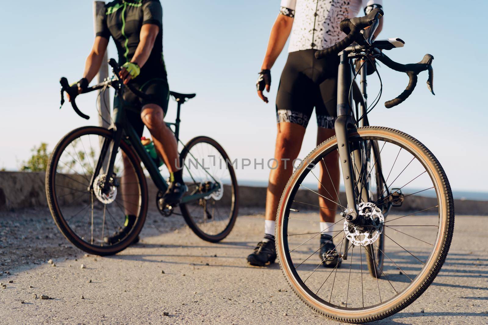 Two male cyclists stand on the road and have a rest by Fabrikasimf