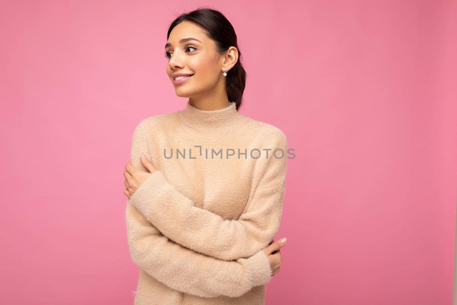 Portrait of beautiful positive cheerful cute smiling young brunette woman in casual beige sweater isolated on pink background with copy space.