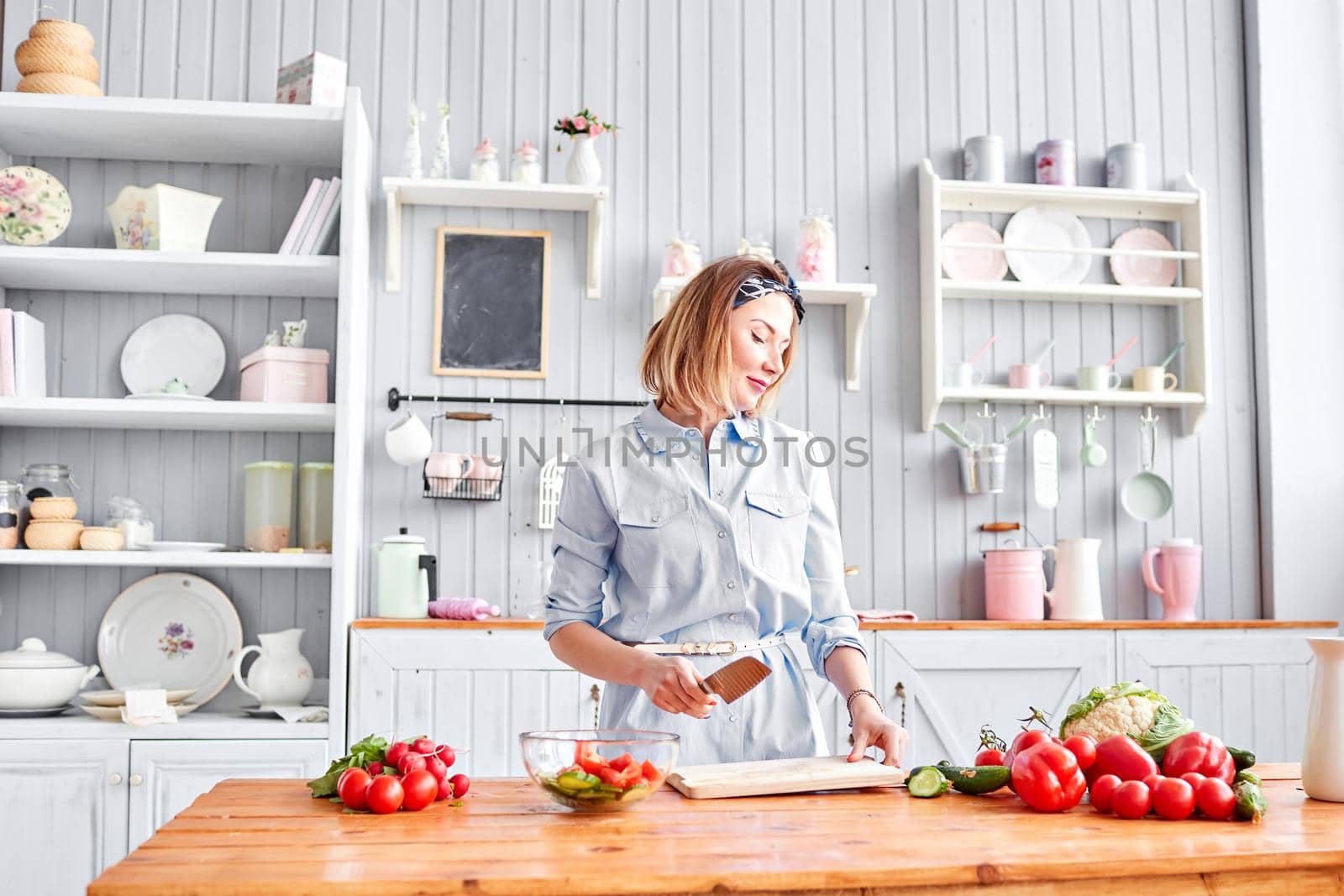 Beautiful young woman is preparing vegetable salad in the kitchen. Healthy Food. Cooking at home. Dieting Concept. by Malkovkosta