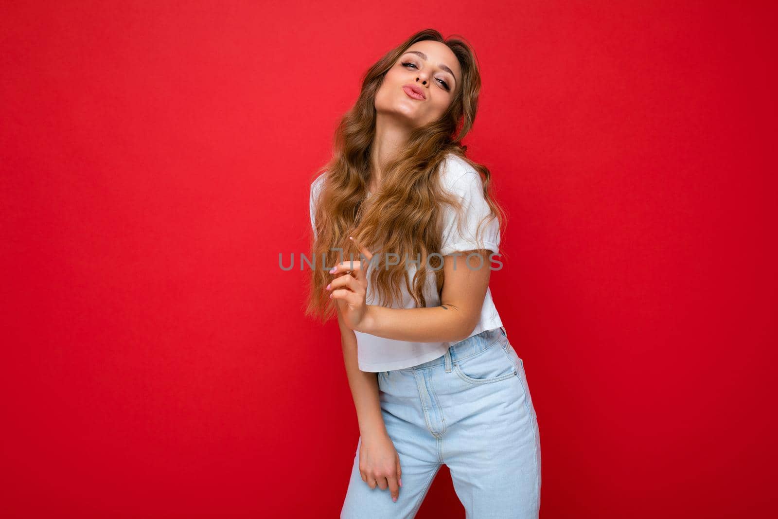 Young beautiful curly blonde woman with sexy expression, cheerful and happy face wearing casual white t-shirt isolated over red background with copy space by TRMK