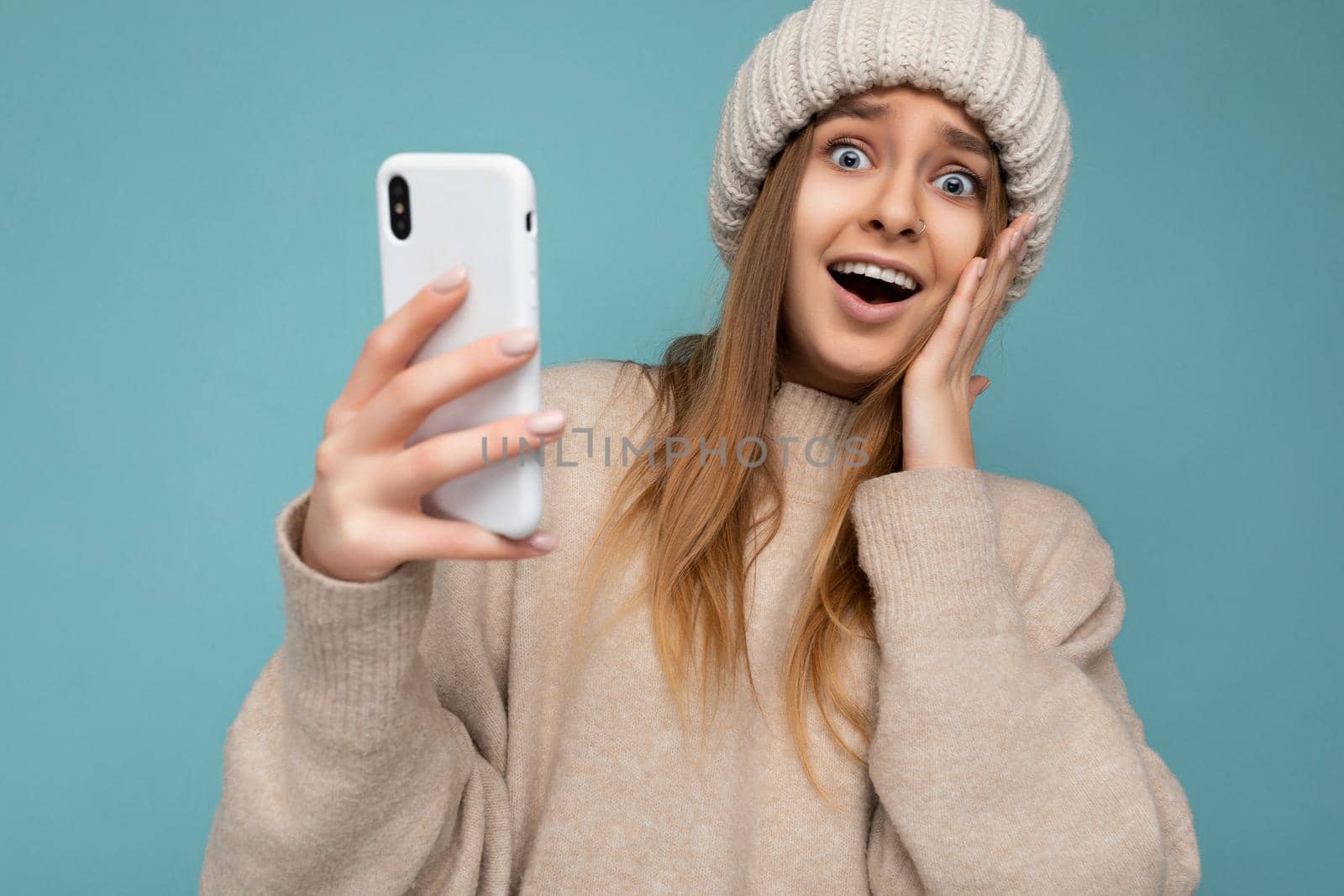 Photo shot of attractive shocked amazed positive good looking young woman wearing casual stylish outfit poising isolated on background with empty space holding in hand and using mobile phone messaging sms looking at camera.