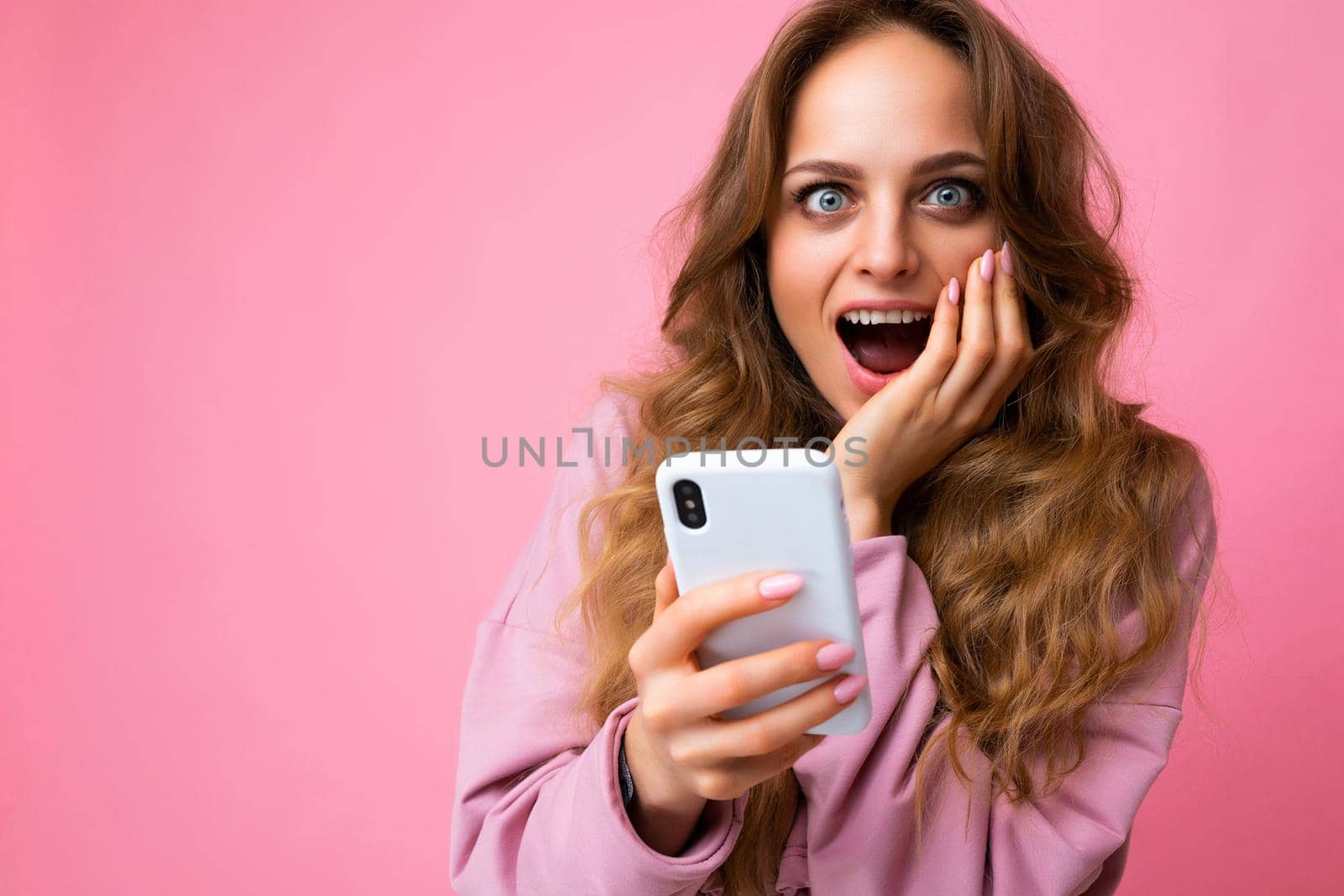 Photo of attractive crazy amazed surprised young woman wearing casual stylish clothes standing isolated over background with copy space holding and using mobile phone looking at camera by TRMK