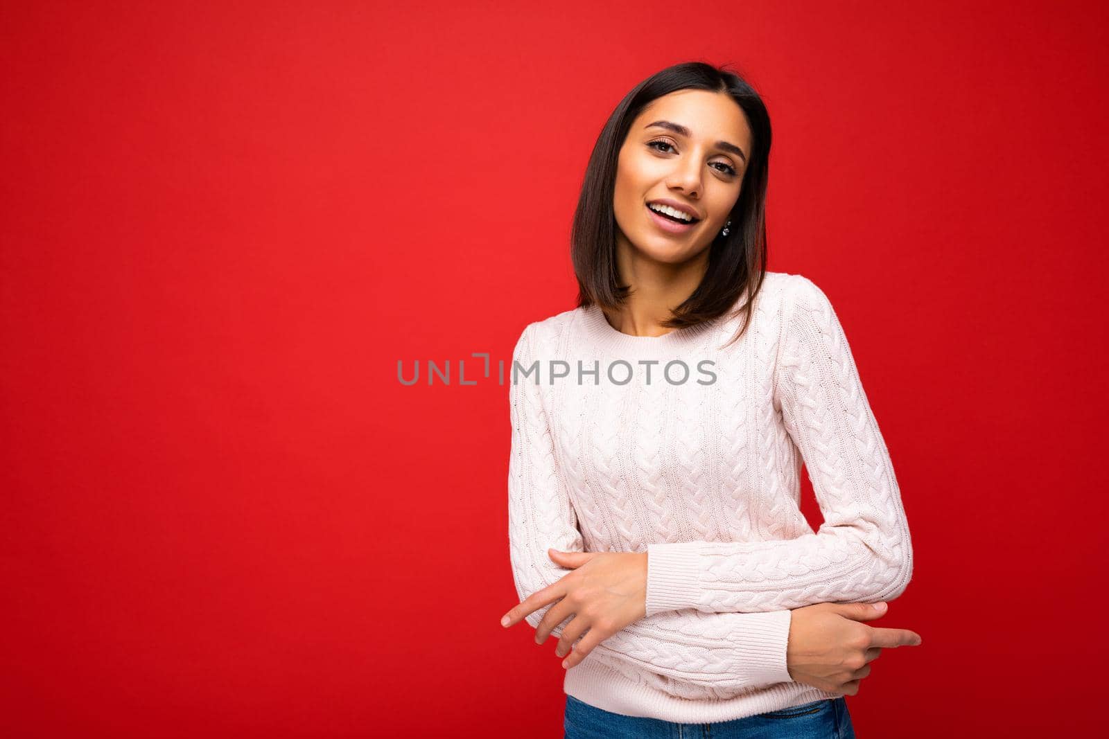 Portrait of positive cheerful cute smiling young brunette woman in casual sweater isolated on red background with copy space.