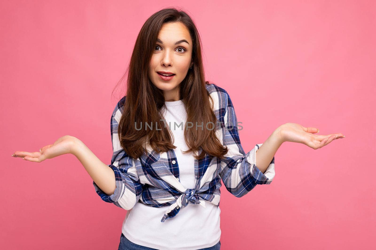 Portrait photo of young thoughtful beautiful brunette woman with sincere emotions wearing stylish check shirt isolated on pink background with copy space and having doubts.