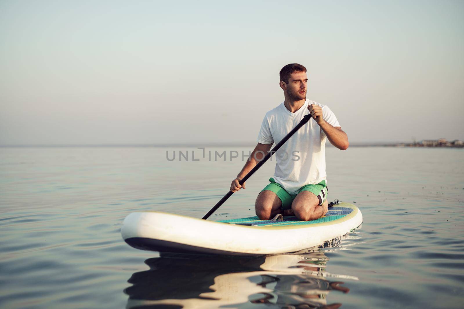 Young man in t-shirt and shorts floating on SUP board at sea