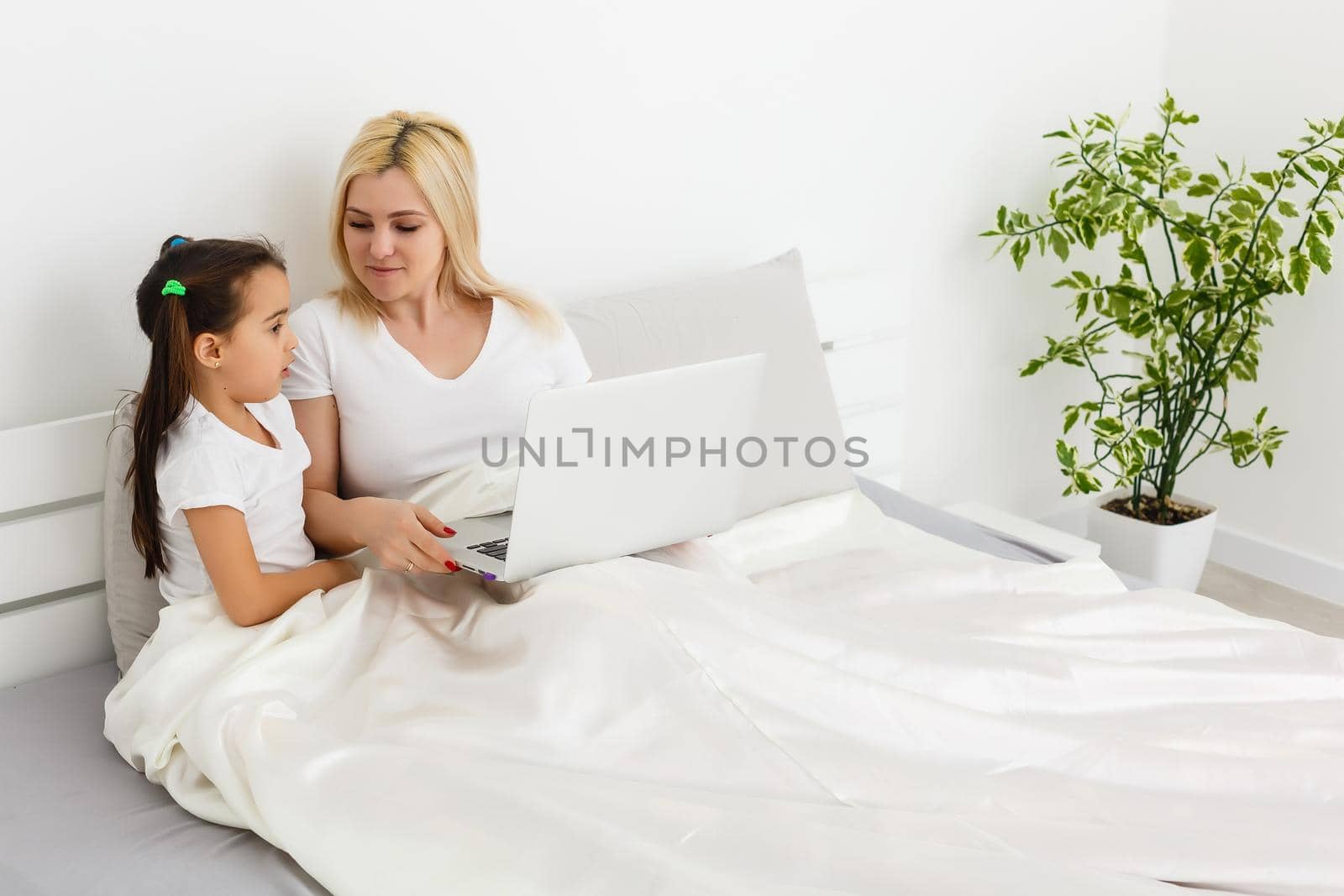 Young mother with toddler child working on the computer from home in bed by Andelov13