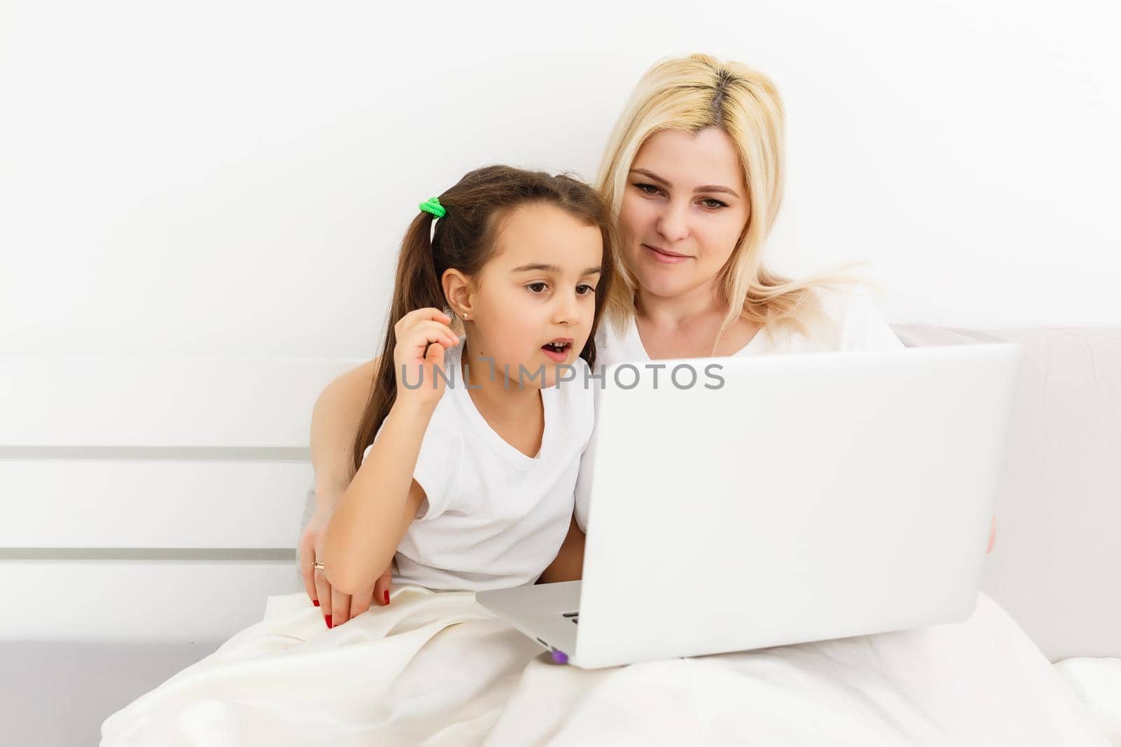 Young mother with toddler child working on the computer from home in bed