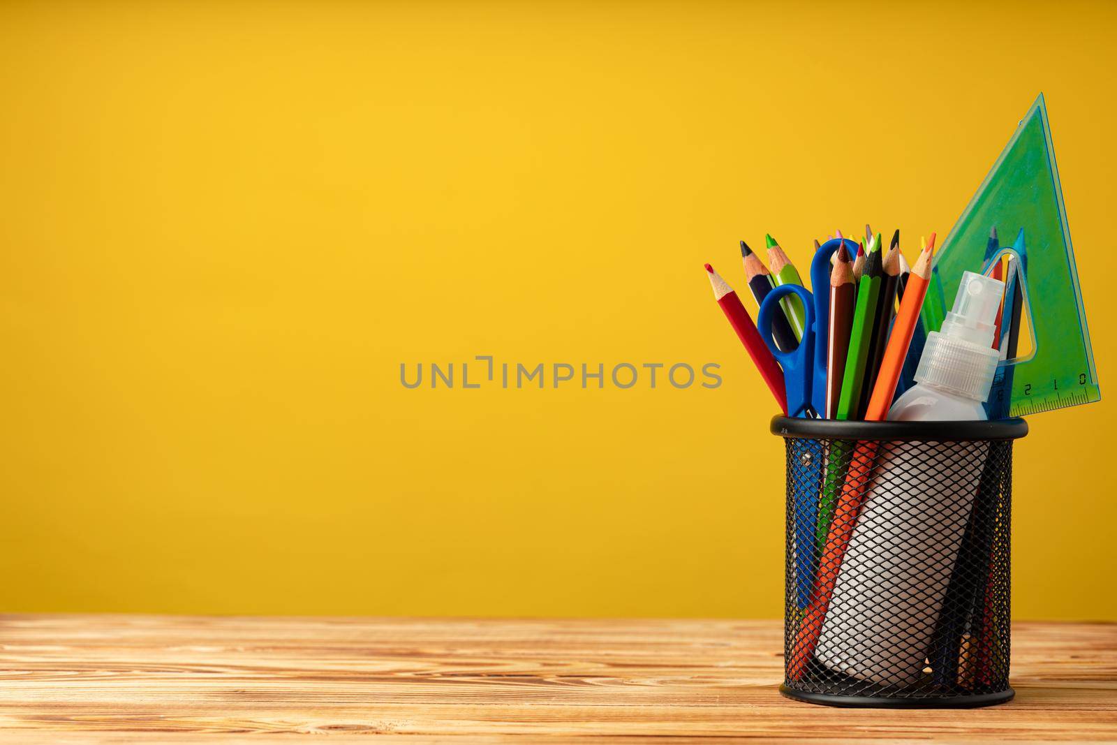 School supplies on wooden desk against yellow background front view