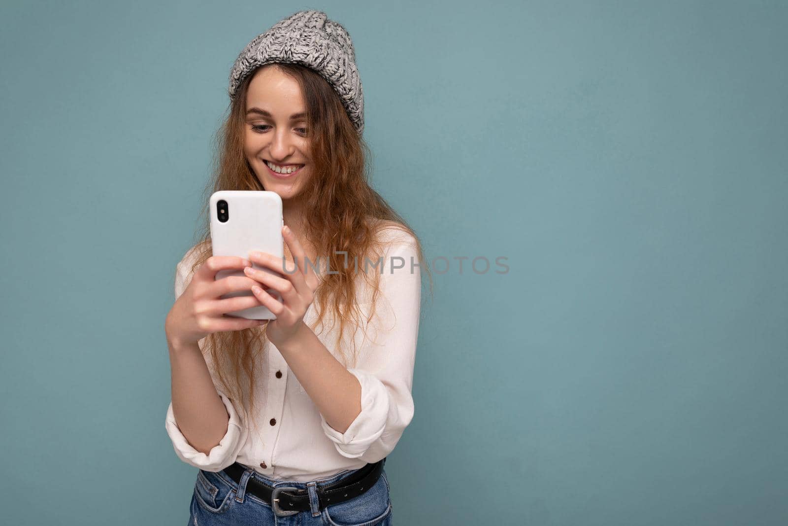 Beautiful young woman wearing casual clothes standing isolated over background surfing on the internet via phone looking at mobile screen.