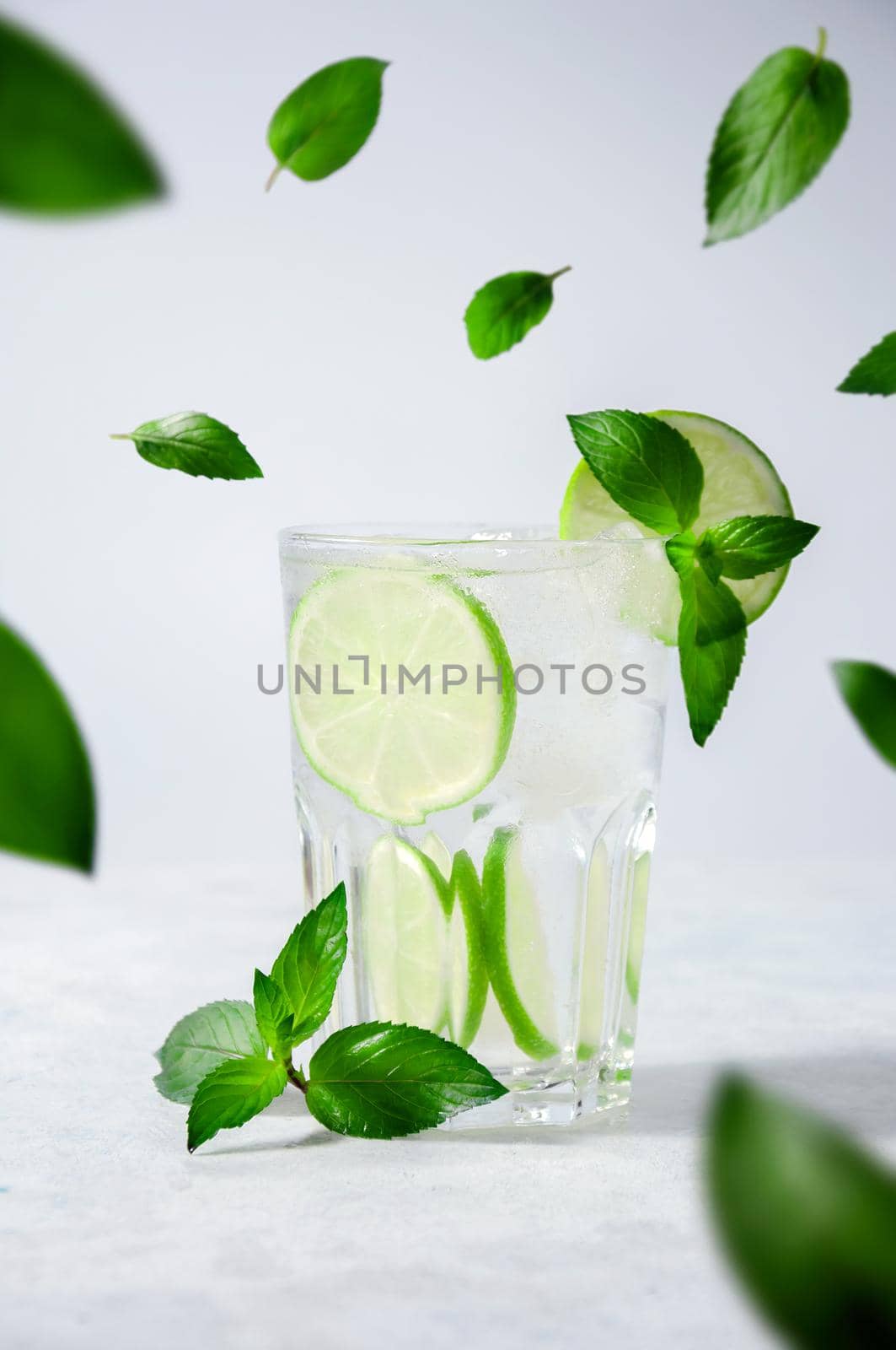 Cocktail Mojito or Lemonade with Lime, Mint and Ice on Light Background. Concept Fresh Summer Drinks.