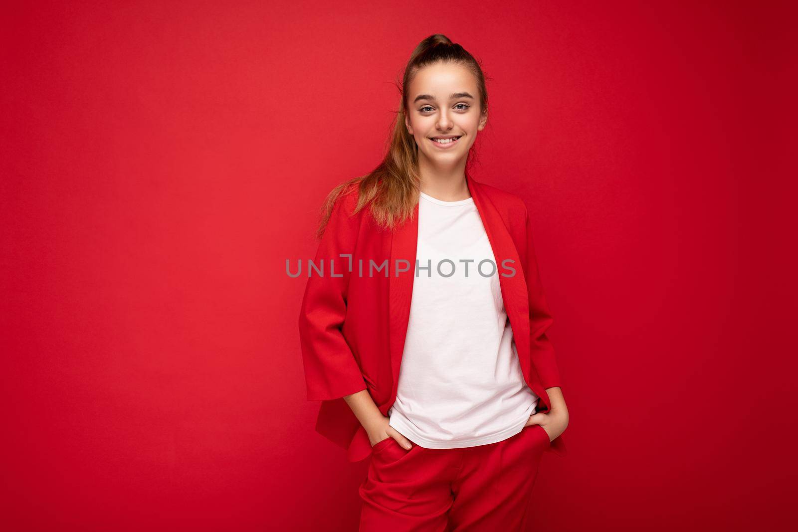Photo shot of beautiful happy smiling brunette little girl wearing trendy red jacket and white t-shirt for mockup standing isolated over red background wall looking at camera by TRMK