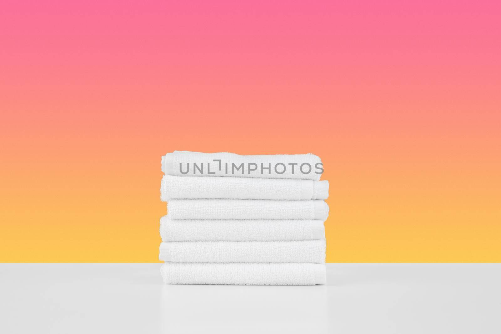 Stacked clean towels on white table against color background, front view