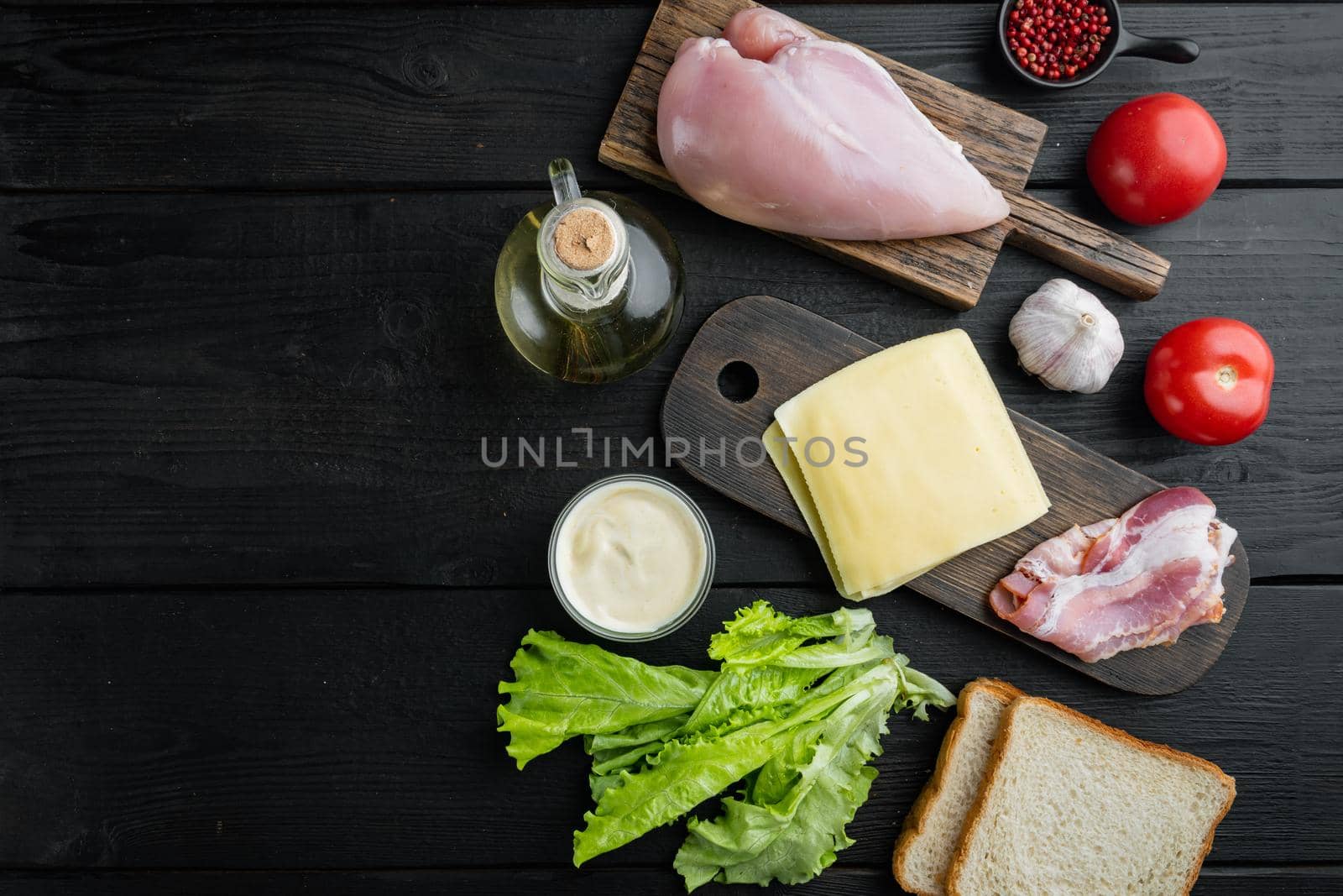 Ingredients for sandwich, bacon, cheese, tomato, chicken meat, lettuce, sauce, on black wooden table, top view with copy space for text