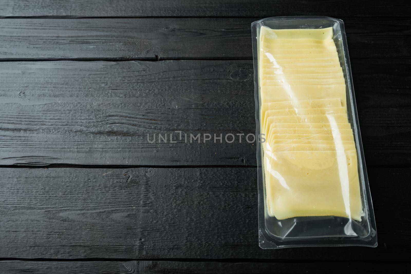 Slices of american cheese plastic pack, on black wooden table with copy space for text