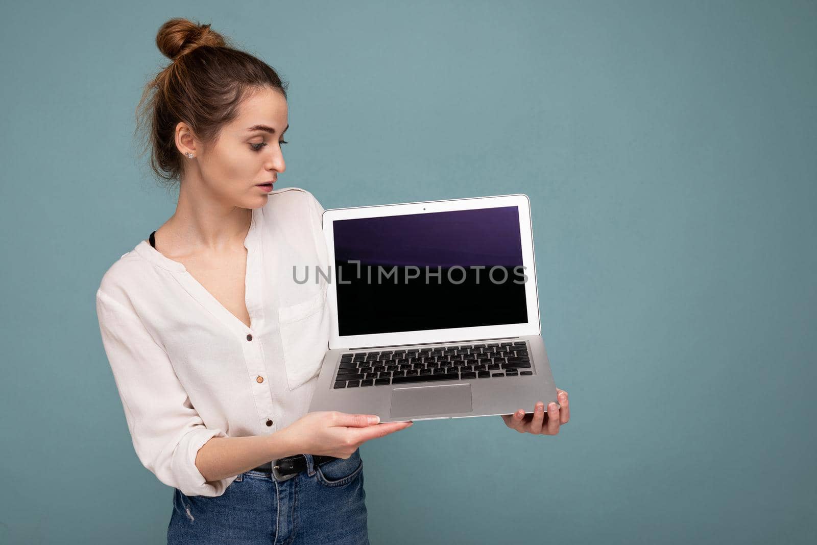 side profile portrait of Beautiful smiling young woman holding netbook computer looking at monitor wearing white shirt isolated on blue background. copy space
