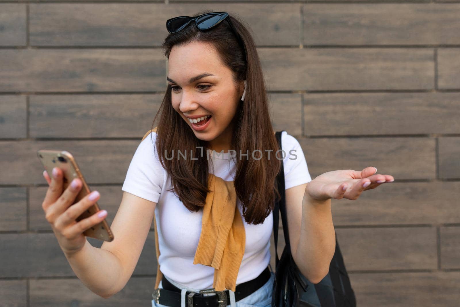 Surprised young woman posing isolated on brown background, studio portrait. People lifestyle concept. Mock up copy space. Using mobile phone, typing sms message.