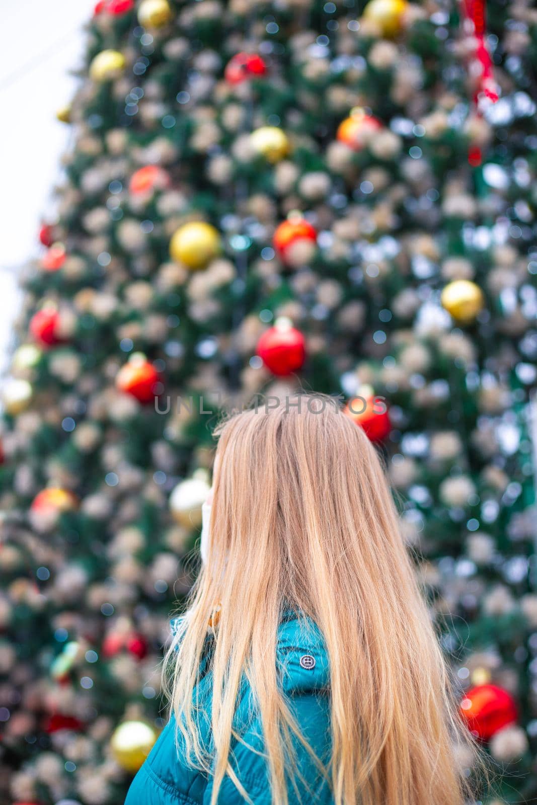 blonde woman on the background of a festive fir tree, view from the back. Celebrating Christmas and New Year during the coronavirus pandemic.