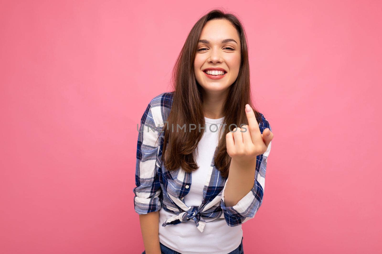 Shot of young happy smiling beautiful brunette lady with sincere emotions wearing trendy check shirt isolated on pink background with empty space.