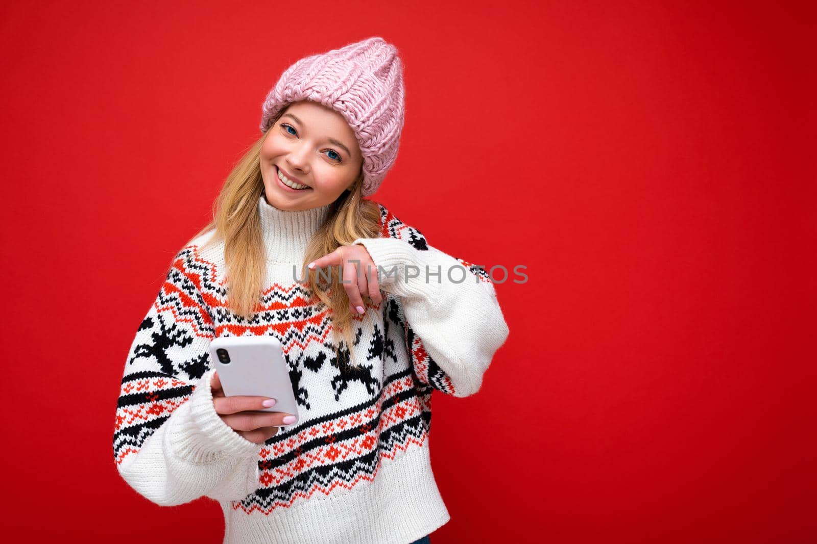 Photo shot of attractive smiling positive good looking young woman wearing casual stylish outfit poising isolated on background with empty space holding in hand and using mobile phone messaging sms looking at camera.