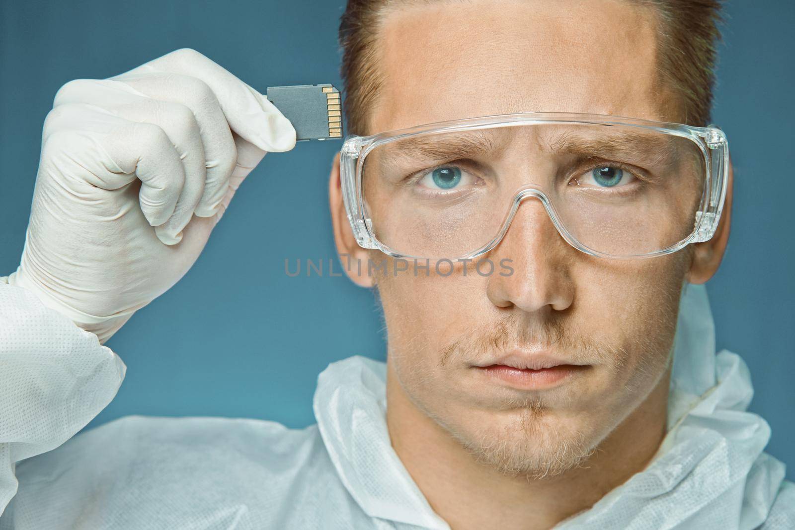 Serious young man in futuristic clothing holding a memory card near his head, concept of modern technologies