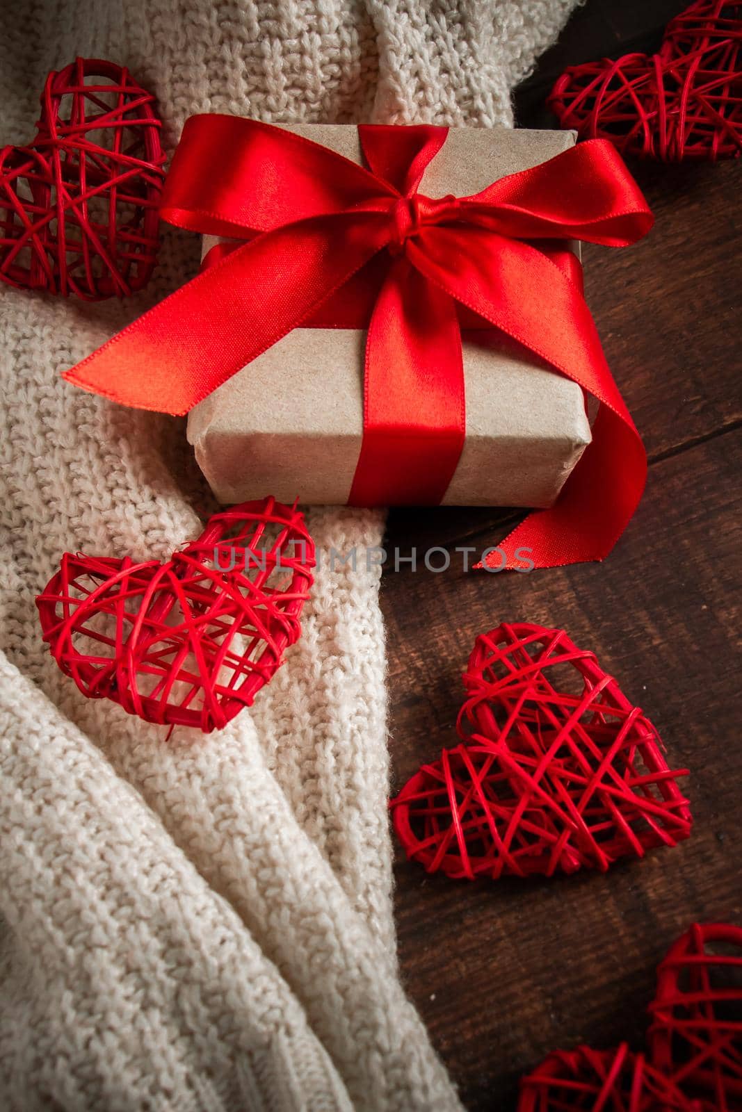 Gift box with red ribbon and hearts. Gift for Valentine's Day in a box with a red ribbon on the background of hearts and a cozy knitted pullover, vertical photo