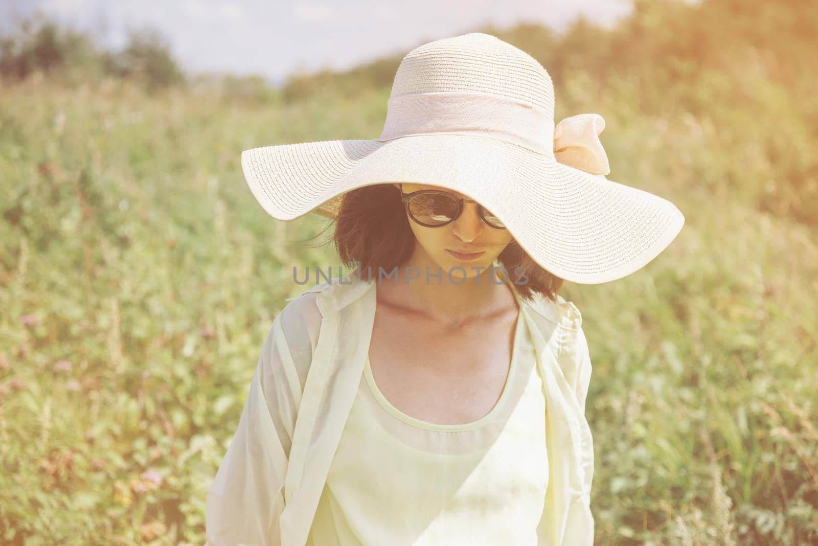 Beautiful fashionable young woman in sunglasses and a hat resting in summer park. Image with sunlight effect