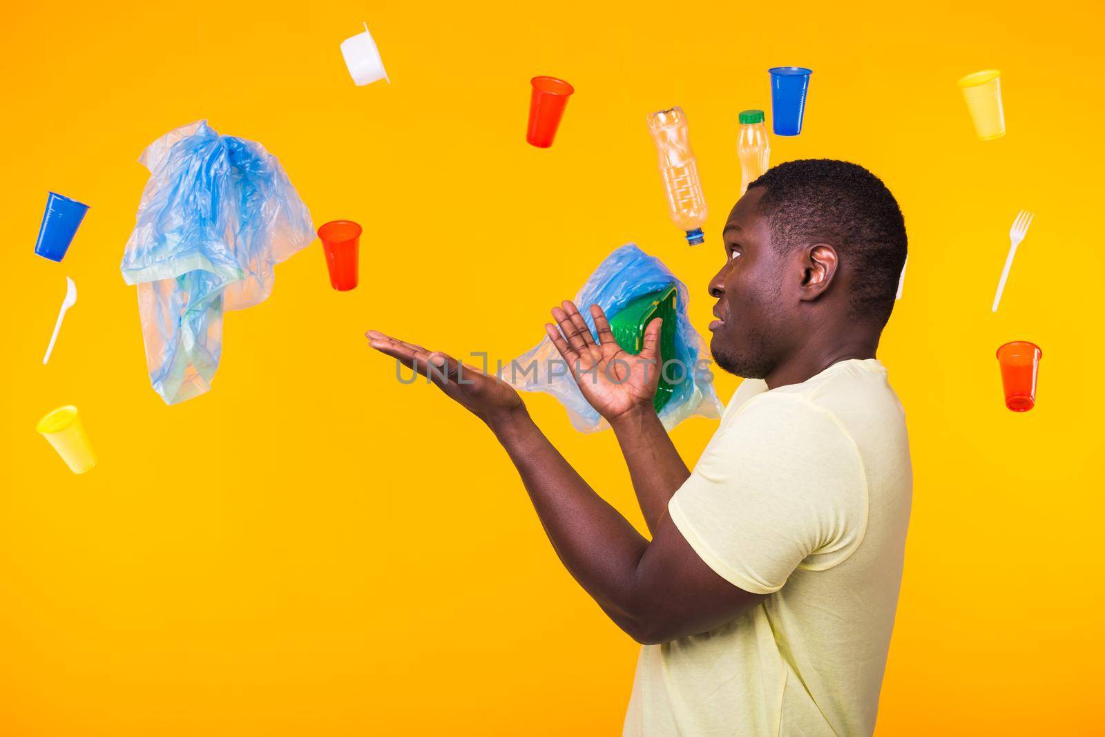 World Environment Day, plastic recycling problem and environmental disaster concept - Surprised african american man looking on trash on yellow.