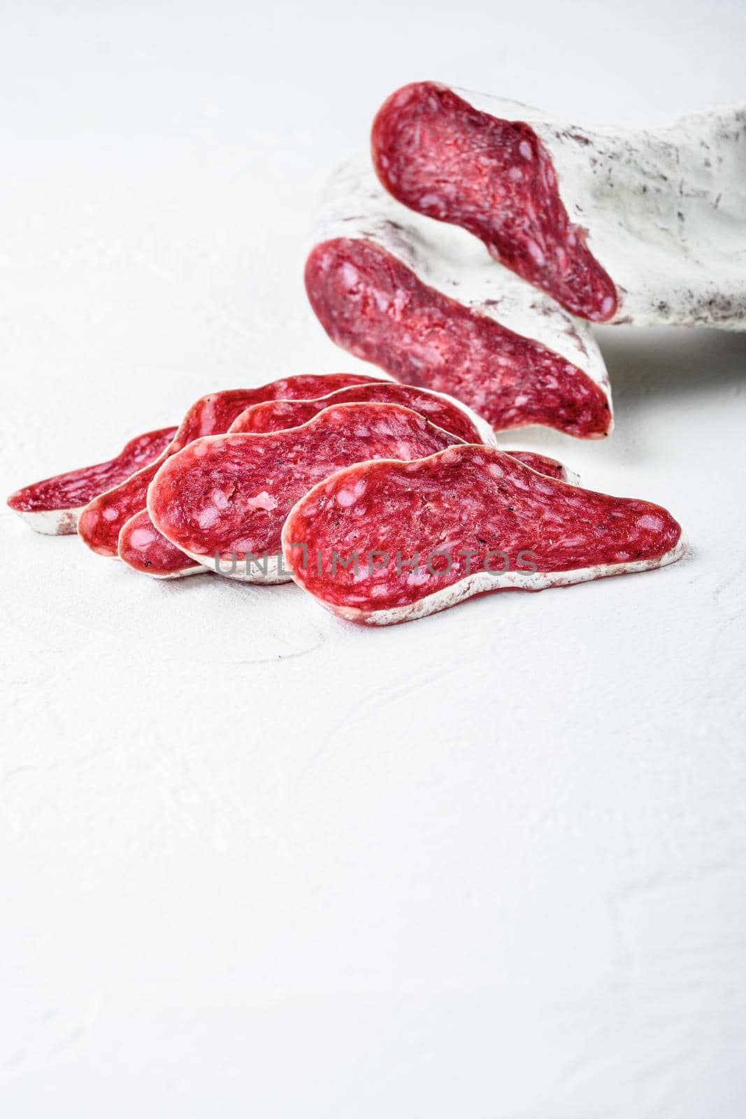 Sliced cuts of longaniza, dry cured spanish sausage on white textured background with space for text.