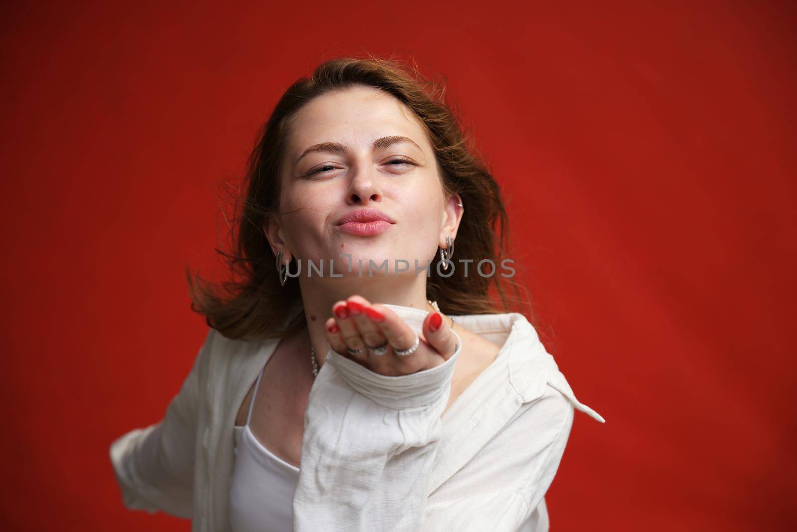 portrait of a model young girl sends a kiss on a red background in the studio by chichaevstudio