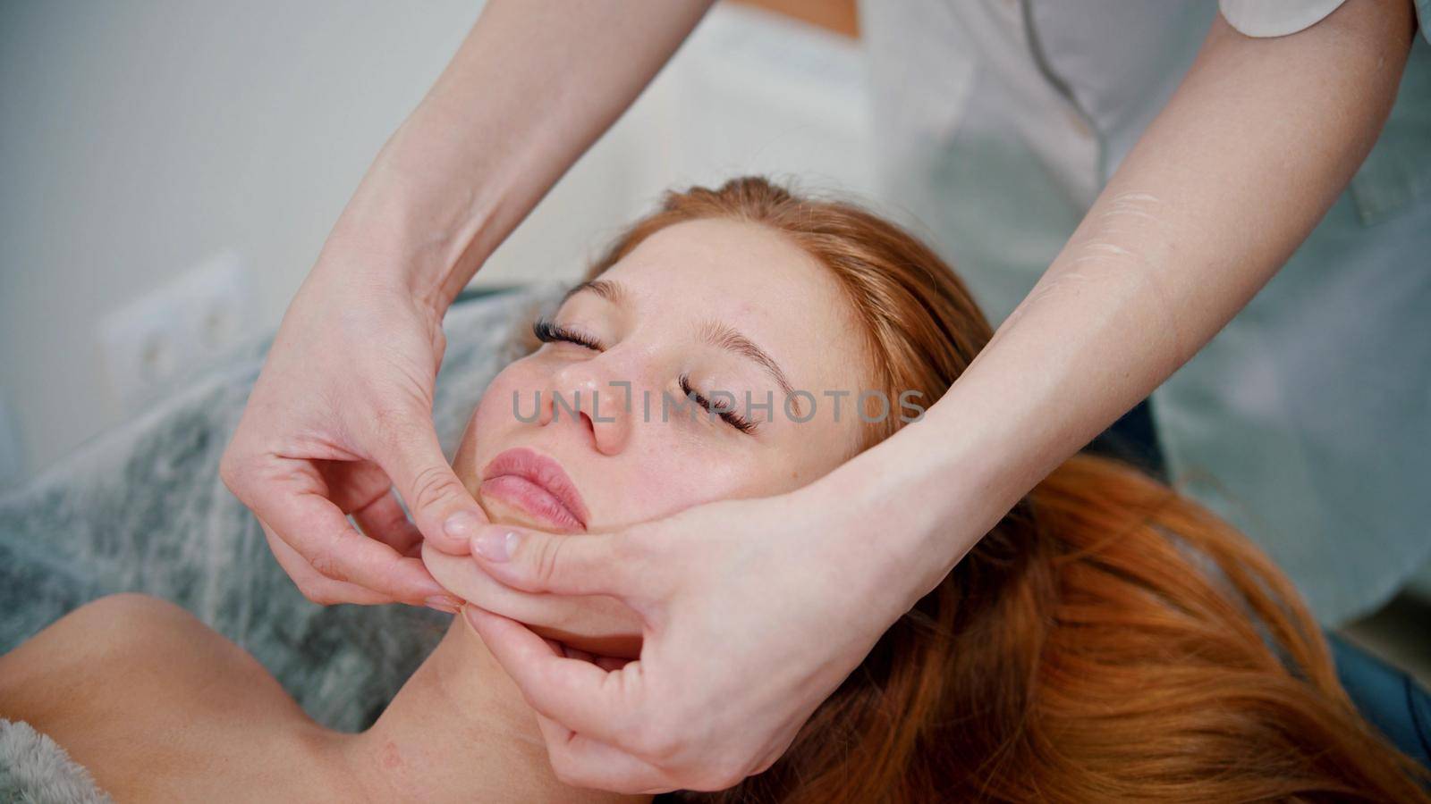 Massage - woman massage therapist massaging the face of a red-haired woman - indoor