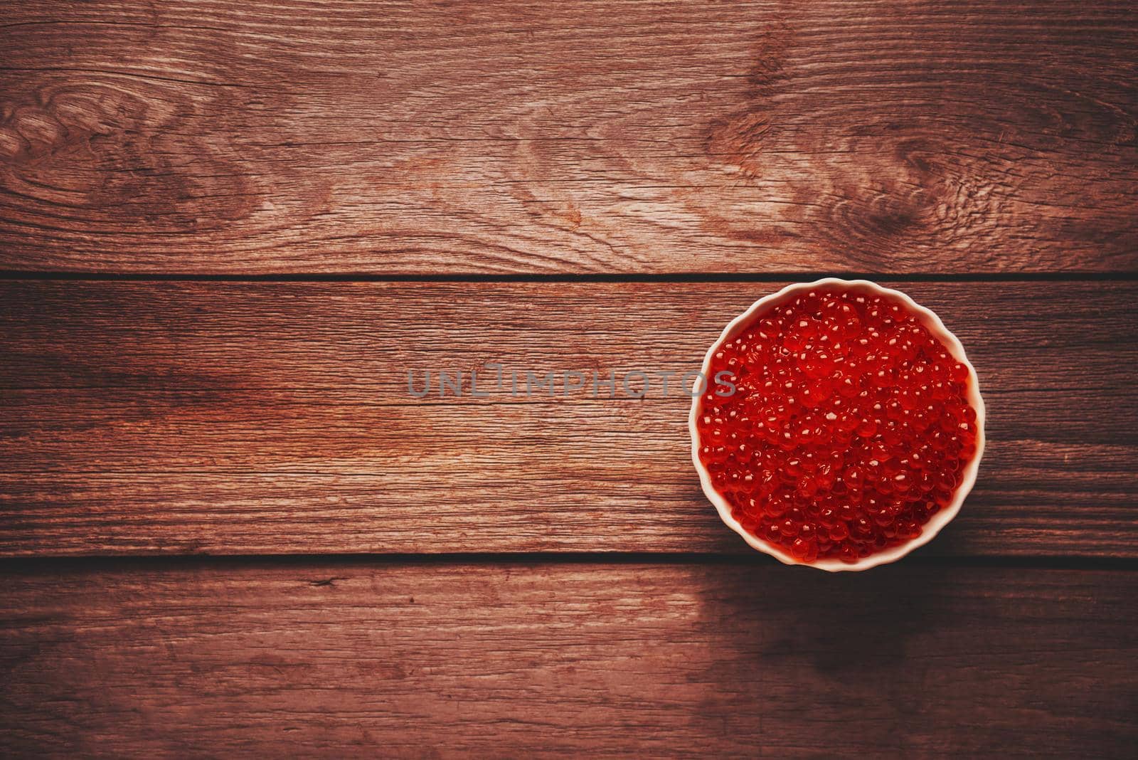 Red salmon caviar in a bowl on wooden background, top view. Space for text in left part of the image