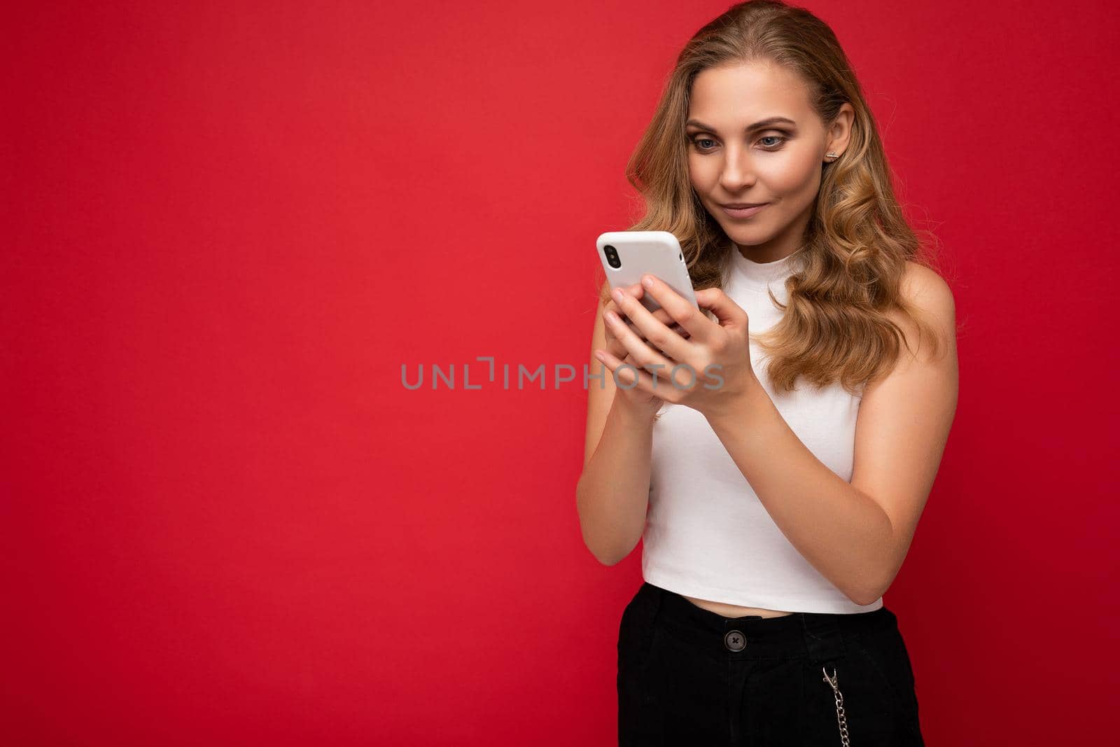 Beautiful young woman wearing casual clothes standing isolated over background surfing on the internet via phone looking at mobile screen.