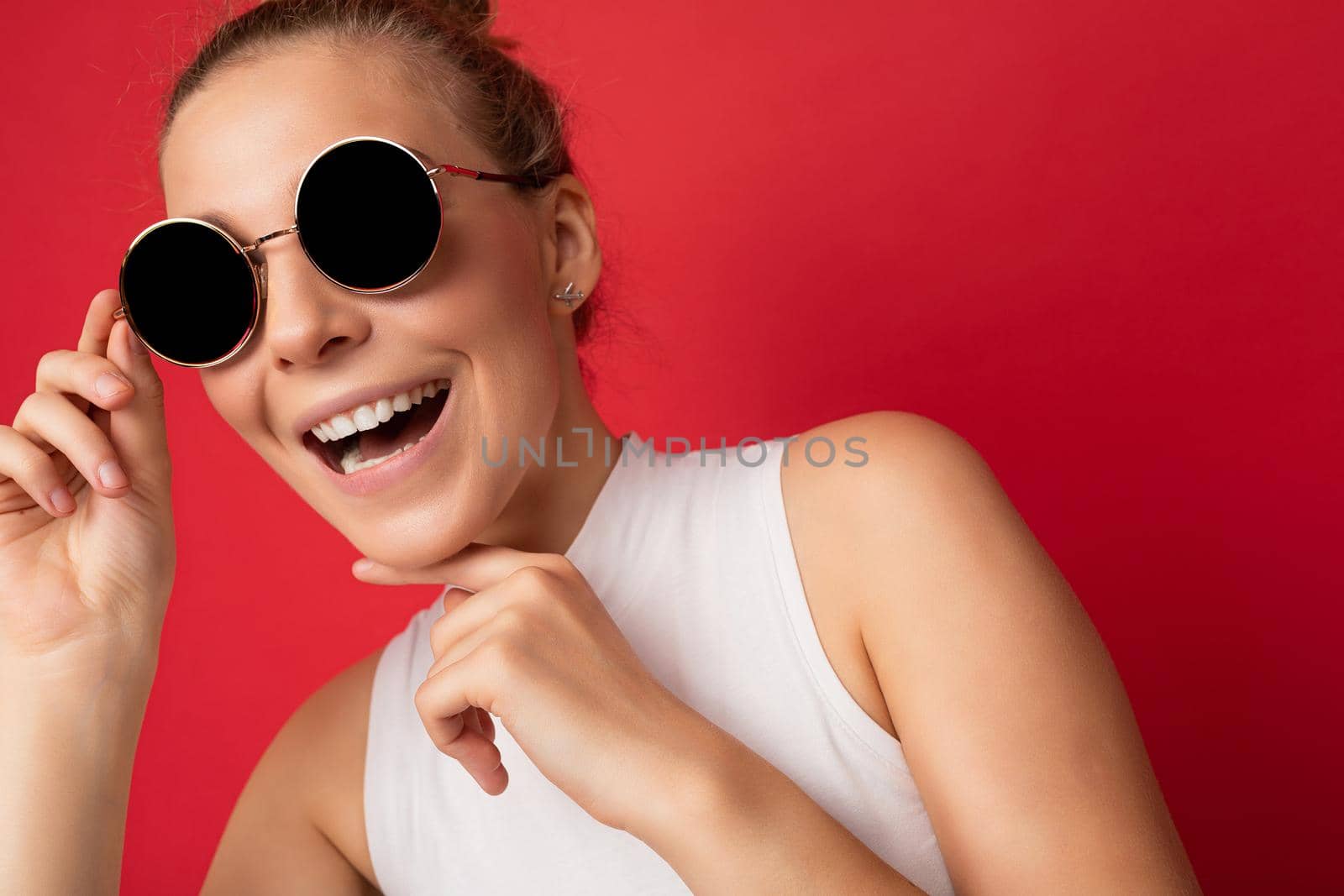 Photo shot of beautiful happy young blonde woman wearing casual clothes and stylish sunglasses isolated over colorful background looking at camera.