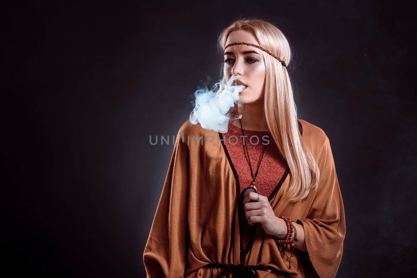 Young woman in the Boho style blowing smoke. The blonde on a dark background