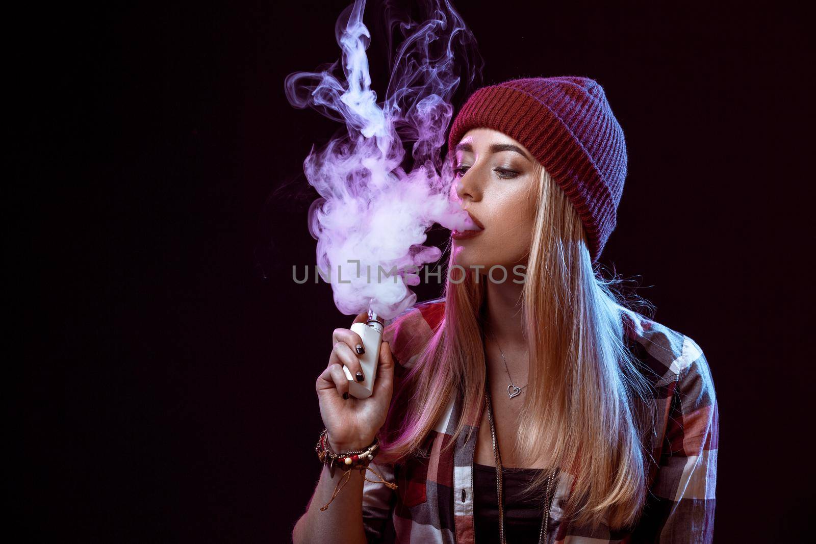 young woman smoking electronic cigarette on black background. Copy space