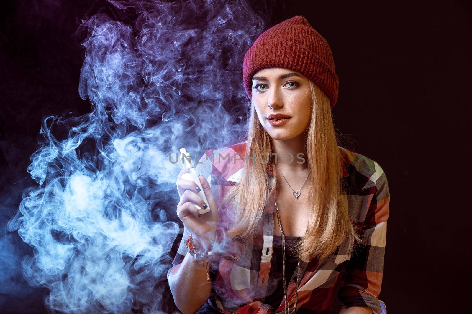 young woman smoking electronic cigarette on black background. woman looking at the camera