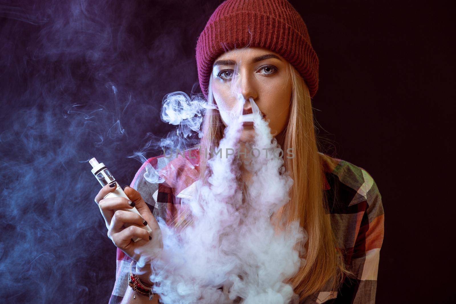 young woman smoking electronic cigarette on black background. woman looking at the camera