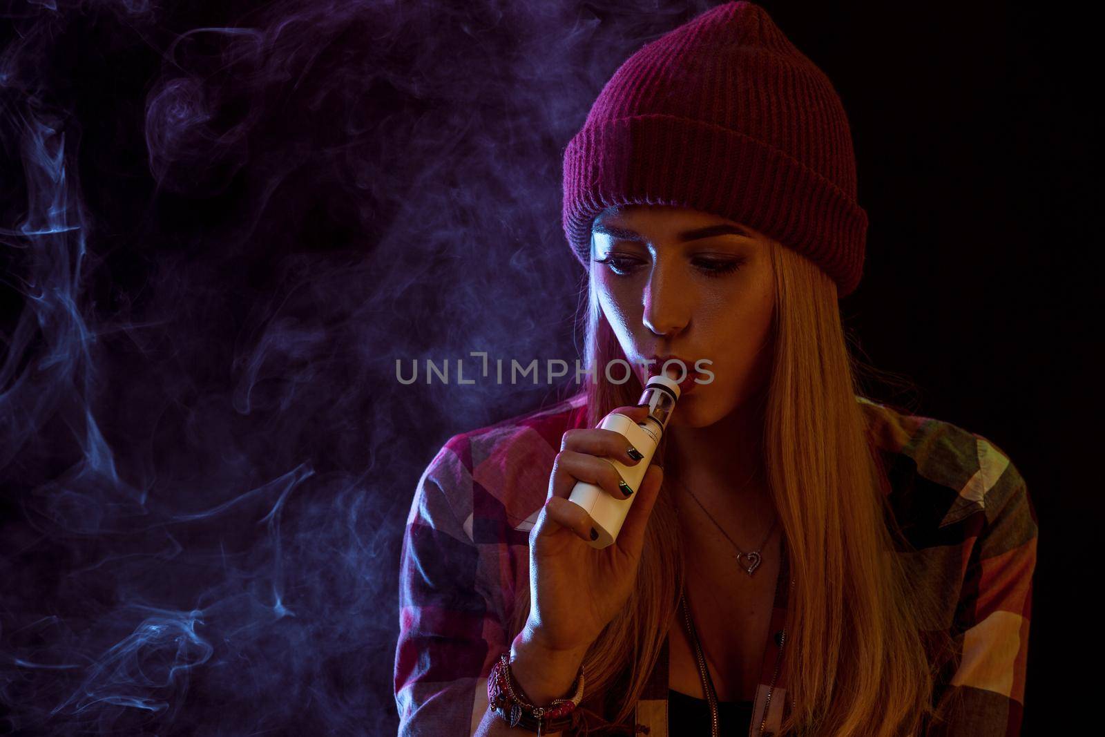 young woman smoking electronic cigarette on black background