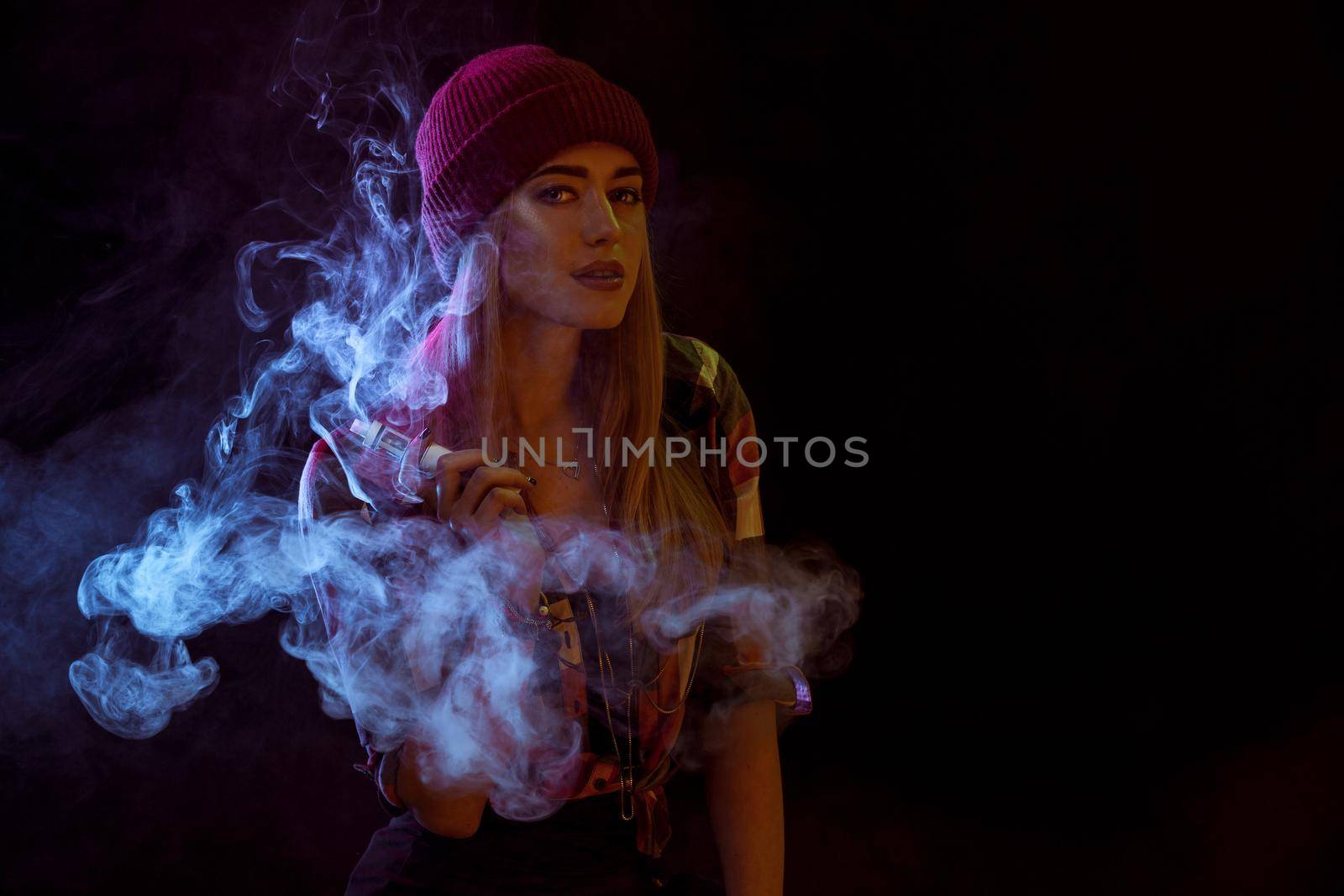 young woman smoking electronic cigarette on black background. woman looking at the camera