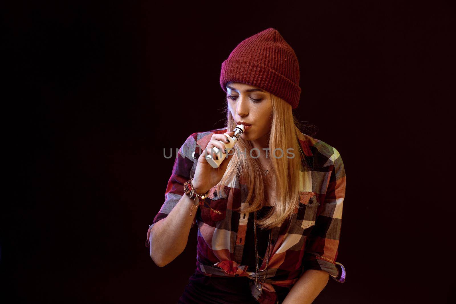 young woman smoking electronic cigarette on black background. Copy space