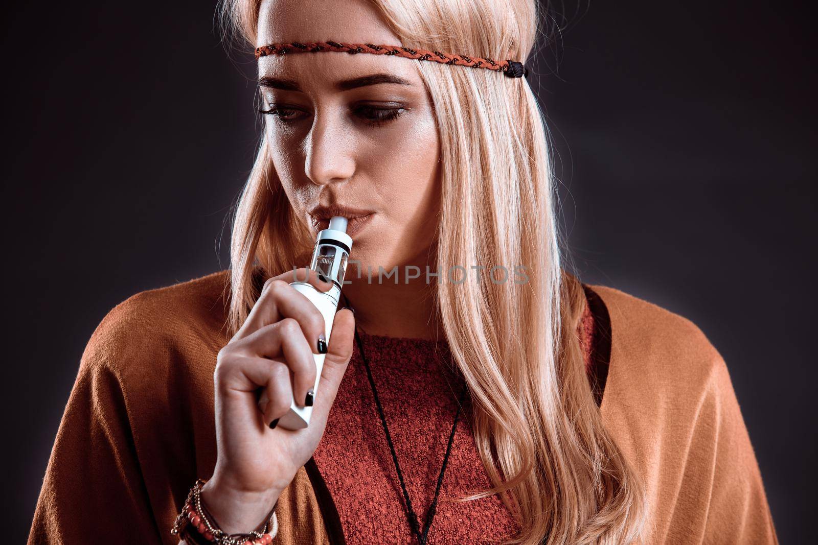 Young woman in the Boho style blowing smoke. The blonde on a dark background. Close-up