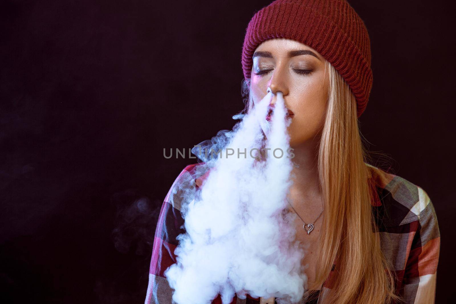 young woman smoking electronic cigarette on black background. Copy space
