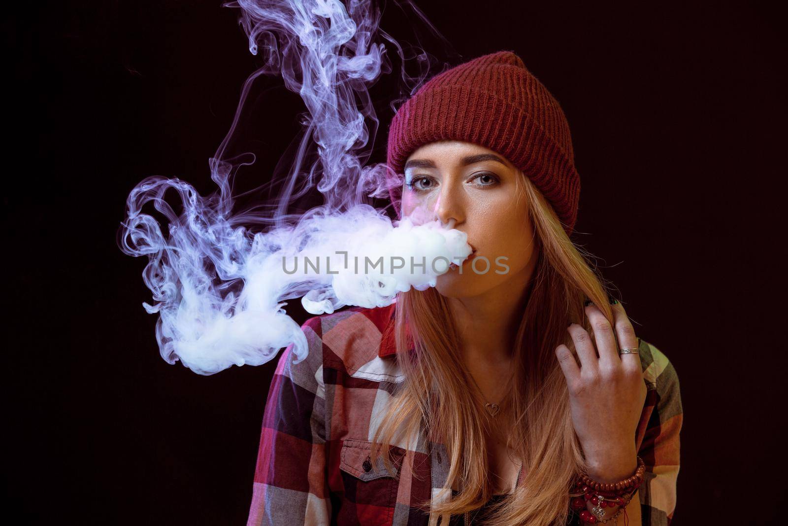 young woman smoking electronic cigarette on black background. woman looking at the camera