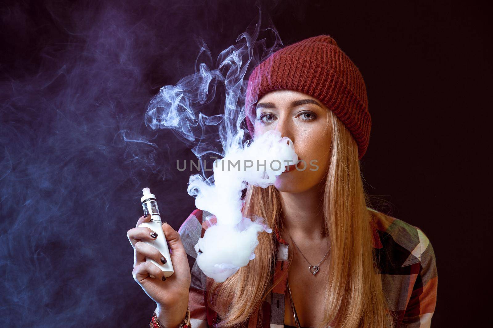 young woman smoking electronic cigarette on black background. woman looking at the camera